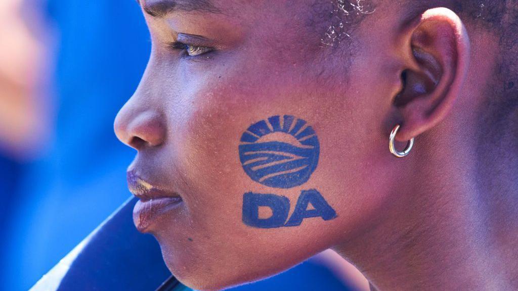 A black woman at a rally with the DA logo stamped on her face.