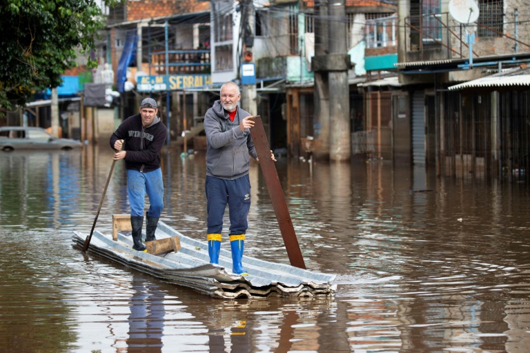Two men paddle a canoe made of zinc tiles and styrofoam down a flooded street in the Vila Farrapos neighborhood in Porto Alegre, Brazil, on May 29, 2024 (SILVIO AVILA)