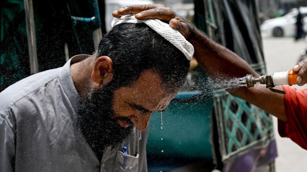 In Karachi, a volunteer sprays water on a bypasser's face to cool off during a hot summer day