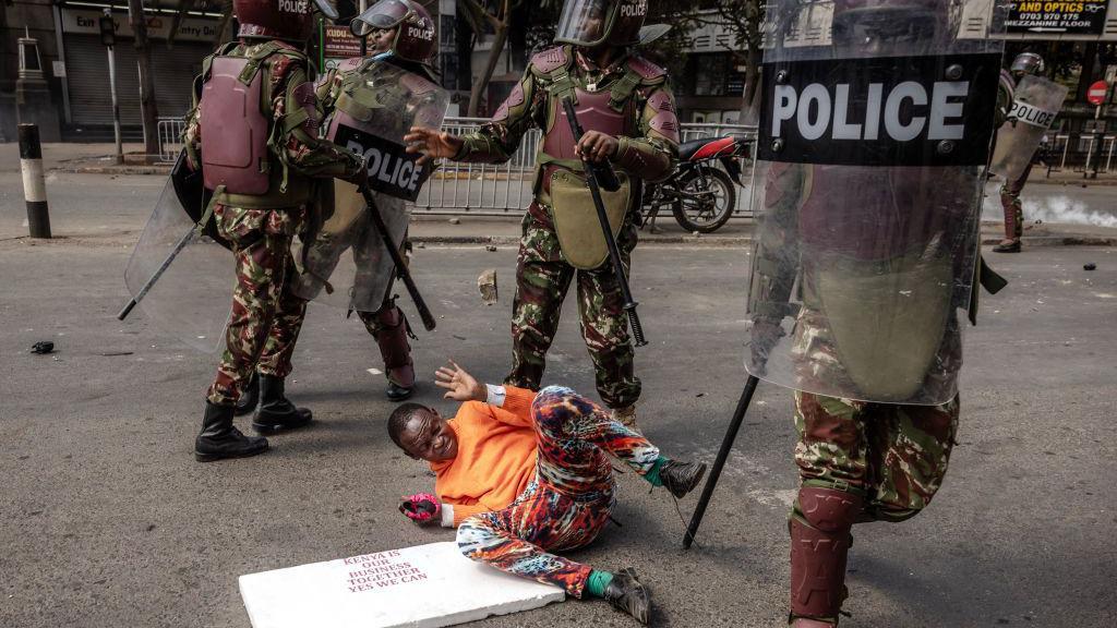 A demonstrator flinches on the ground as riot police stand over him.