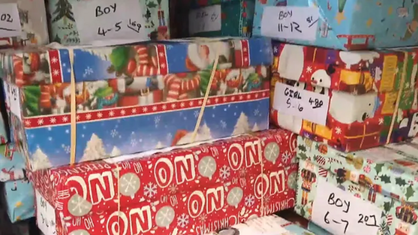 A number of shoe boxes wrapped in Christmas wrapping which have different labels on them such as 'girl, 5-6'