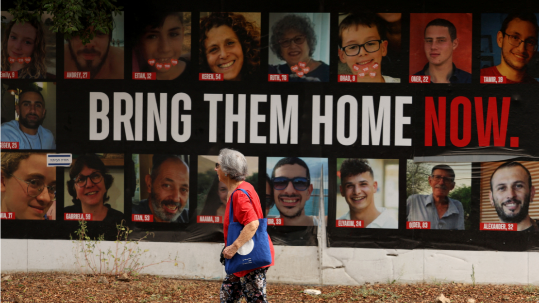 A woman walks past a poster with photos of hostages taken by Hamas