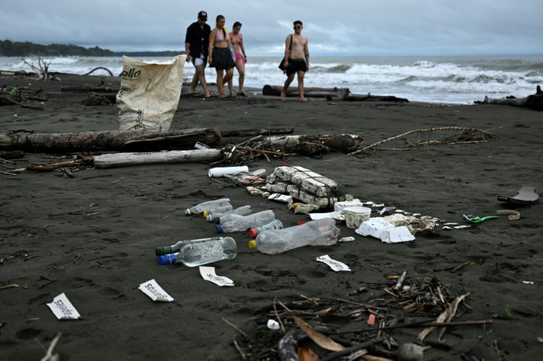 Tourists walk past garbage at la Barra beach in Bahia Malaga, near Buenaventura, department of Valle del Cauca, Colombia, on July 23, 2024. In the Colombian Pacific children trade plastic waste for pseudo coins which they can use to "buy" clothes, books, school supplies or even popcorn. (JOAQUIN SARMIENTO)