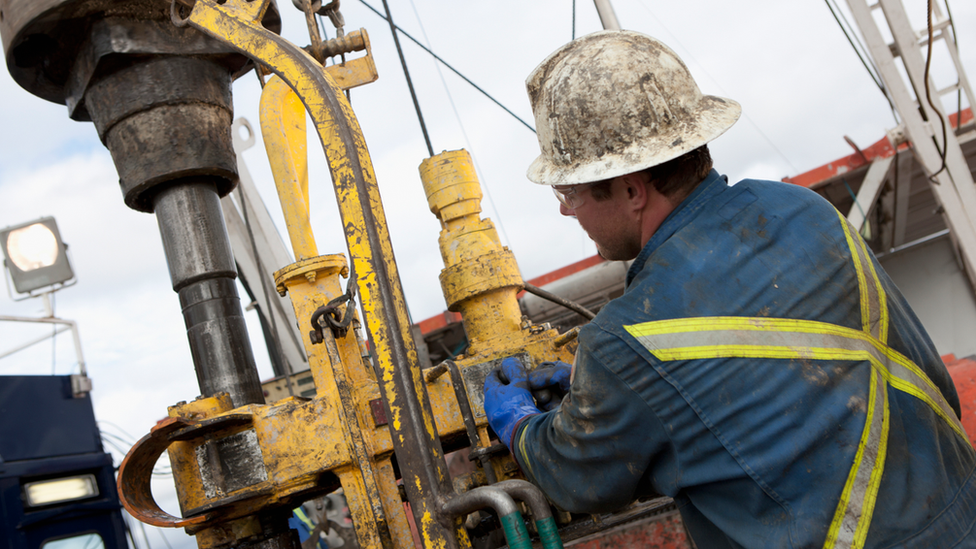 An oil worker operates machinery on an oil rig while wearing a hard hat