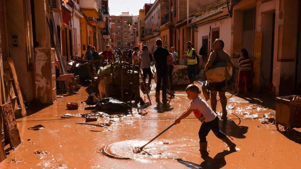 People seen sweeping muddy floodwater from a street in Valencia. Damaged furniture can also be seen piled up.