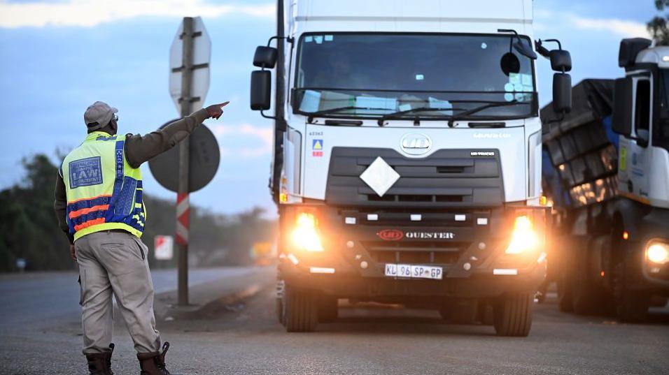 A traffic officer directs a truck driver, waiting to cross South Africa's border into Mozambique, at Lebombo Border control in Komatipoort, South Africa, on Friday, July 14, 2023.